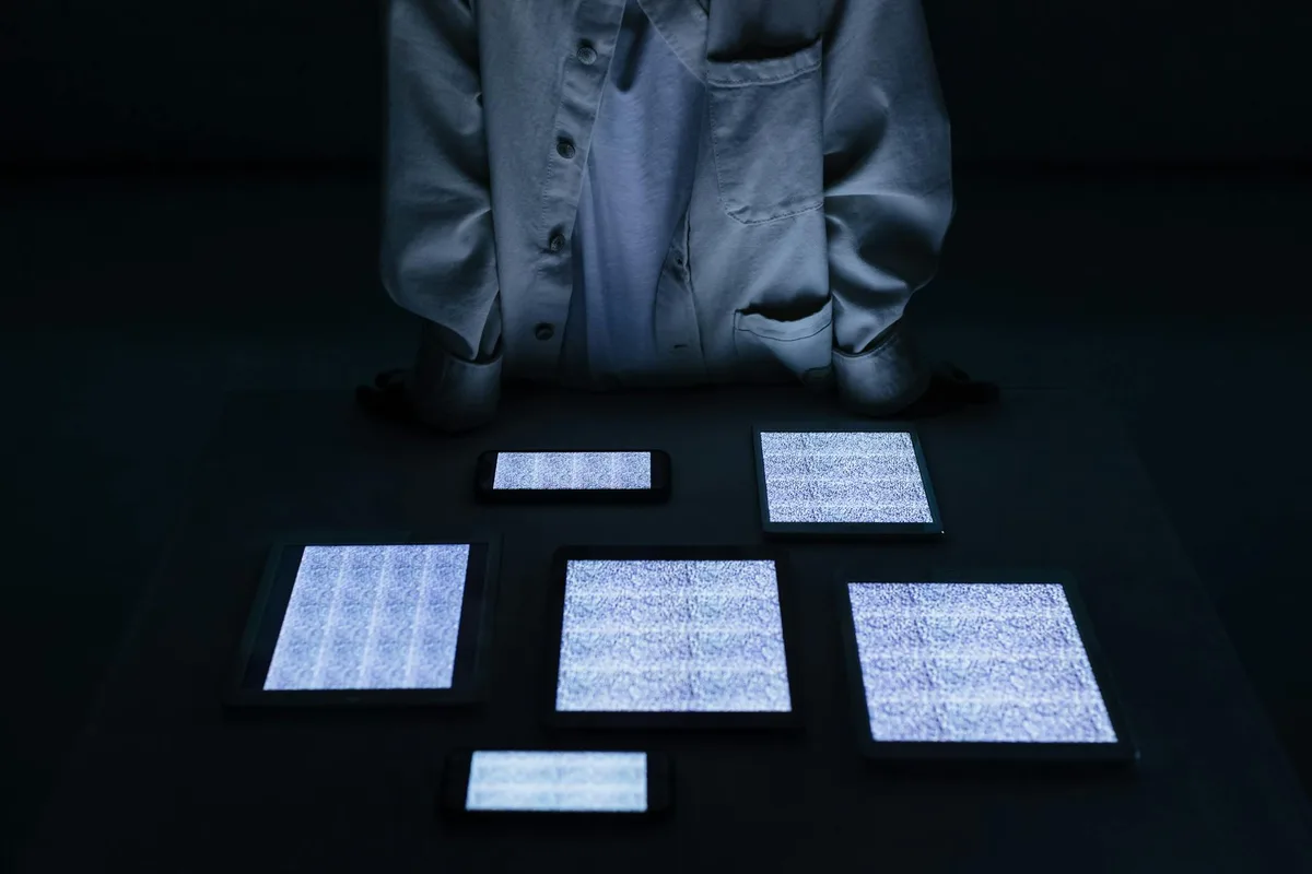 Person in weißem Hemd über Tablets und Handys mit statischen Bildschirmen in dunklem Raum