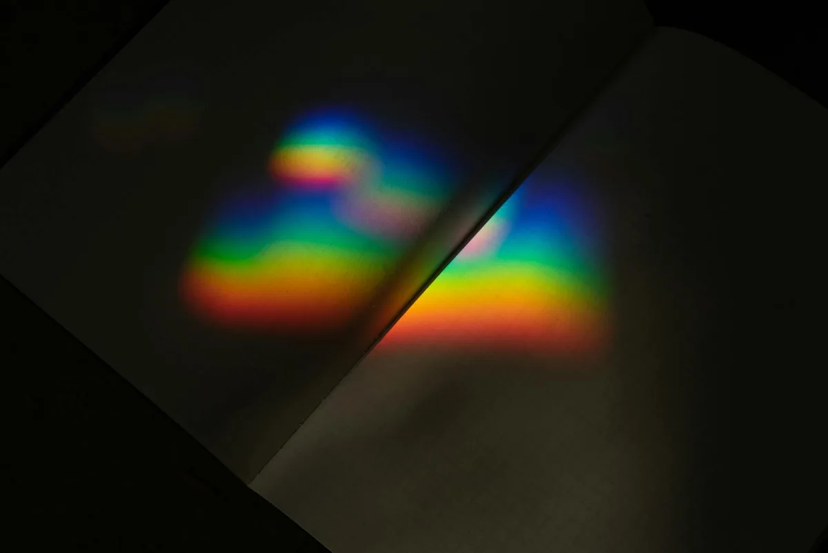 Riflesso prismatico arcobaleno vibrante su pagine di taccuino aperto in illuminazione scura.