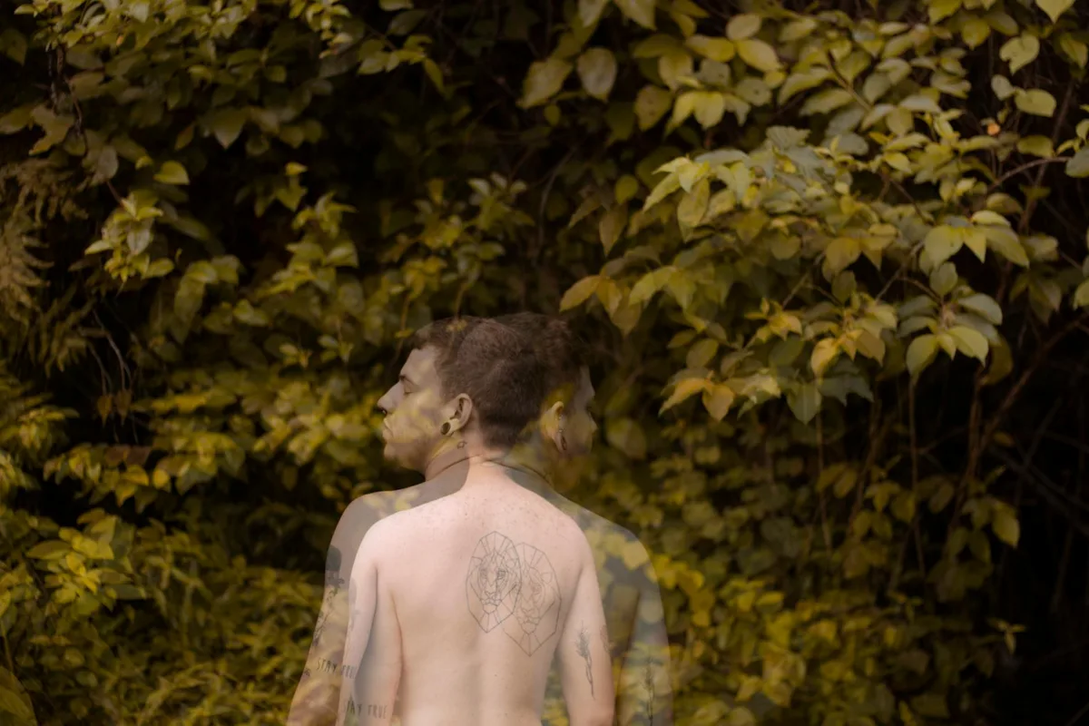 Doppia esposizione artistica di un uomo tatuato tra una rigogliosa vegetazione