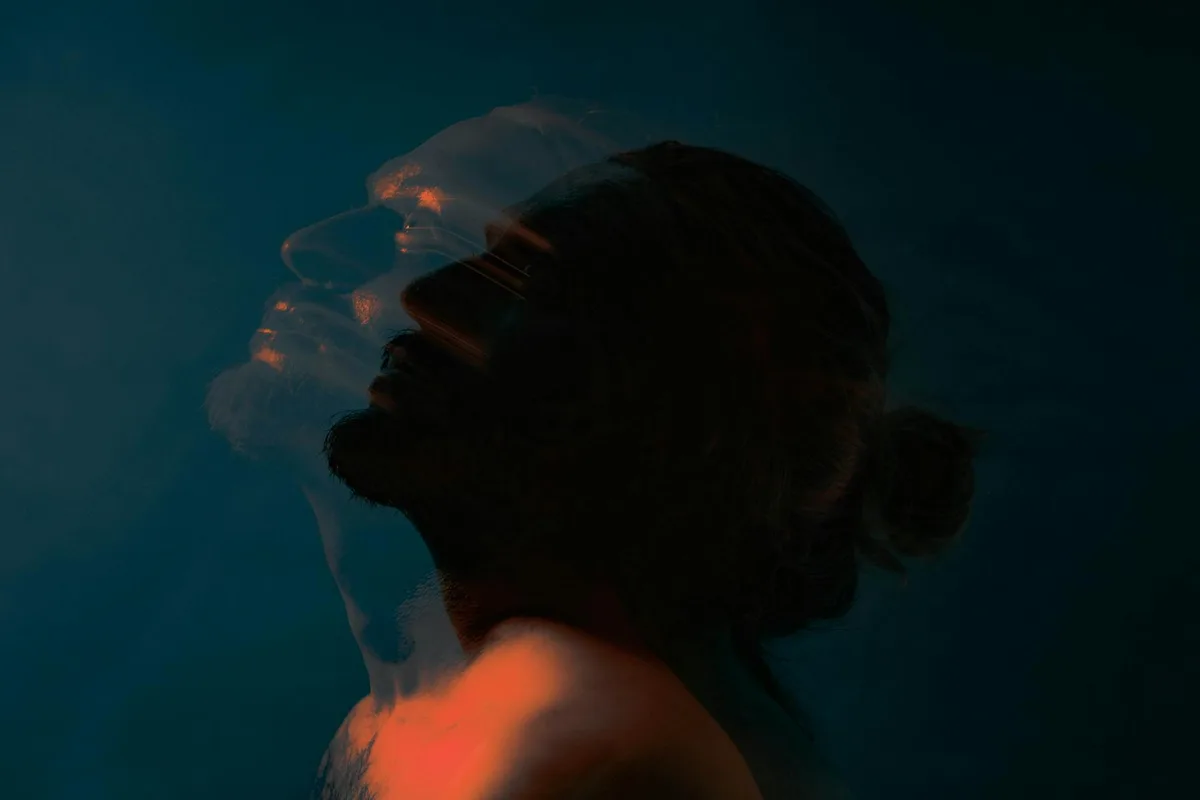 Künstlerische Doppelbelichtung eines bärtigen Mannes in düsterem Licht.