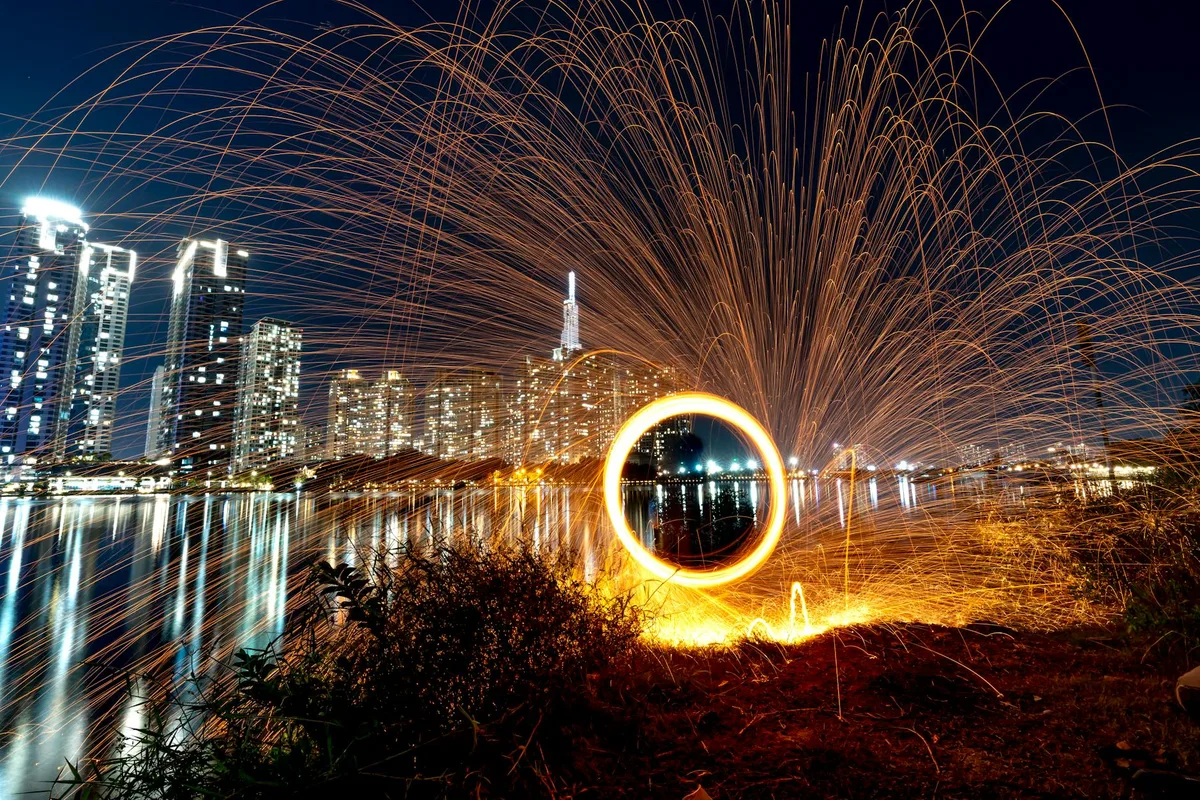 Stahlwollfotografie mit Lichtspuren am urbanen Flussufer bei Nacht