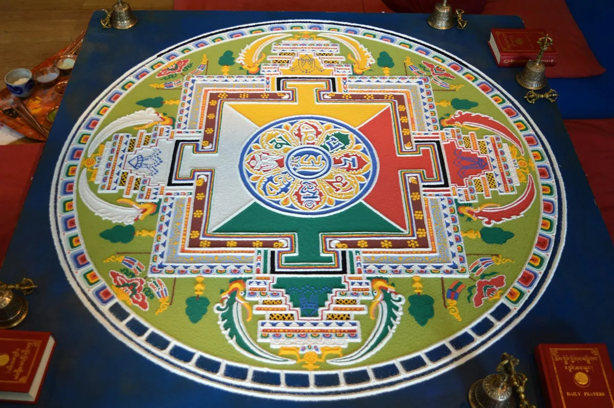 Mandala di sabbia colorato con motivi intricati e simboli in ambiente spirituale