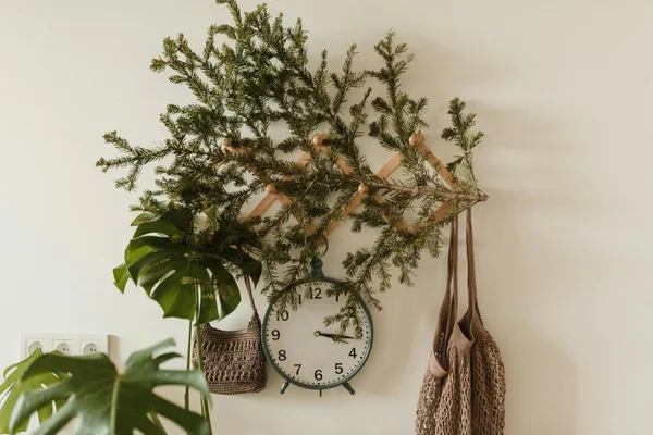 A charming wall display with pine branches, a clock, and woven bags for a rustic touch.