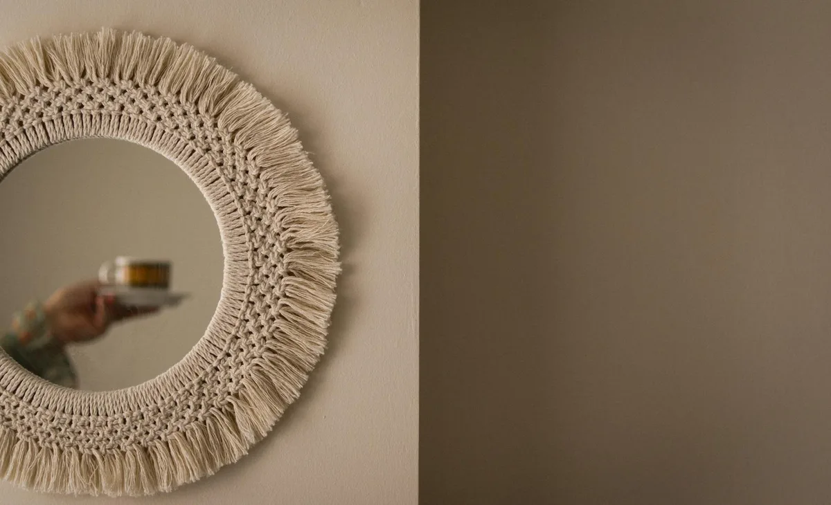 A decorative mirror reflecting a person's hand holding a coffee cup indoors.