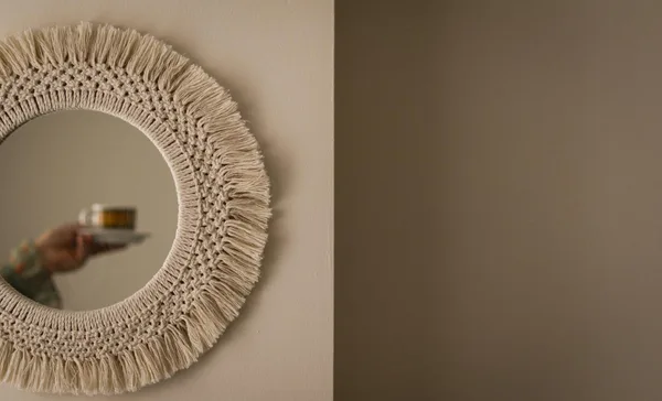 A decorative mirror reflecting a person's hand holding a coffee cup indoors.