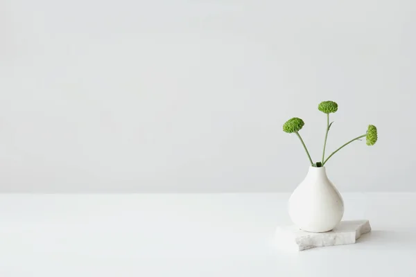 Minimalistische Keramikvase mit grünen Blumen auf weißer Oberfläche, perfekt für Dekoration