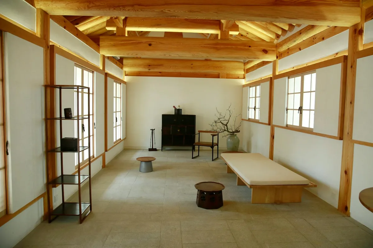 Minimalistischer Raum mit Holzbalken, Regalen und traditioneller Sitzgelegenheit