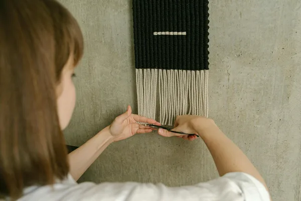 A woman trims fringes on a macramé wall hanging for a stylish home décor touch.
