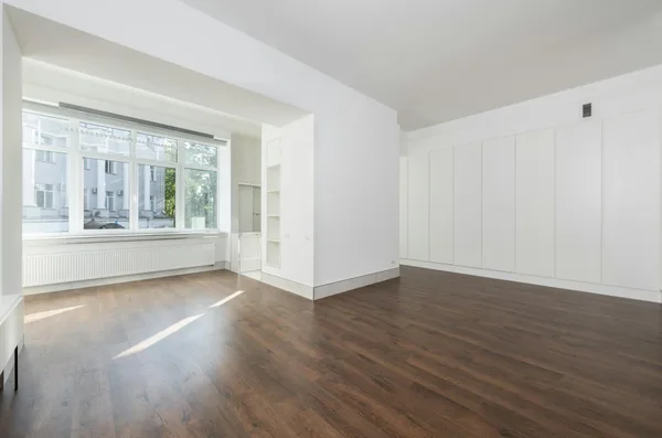 Heller leerer Raum mit großen Fenstern und Holzboden
