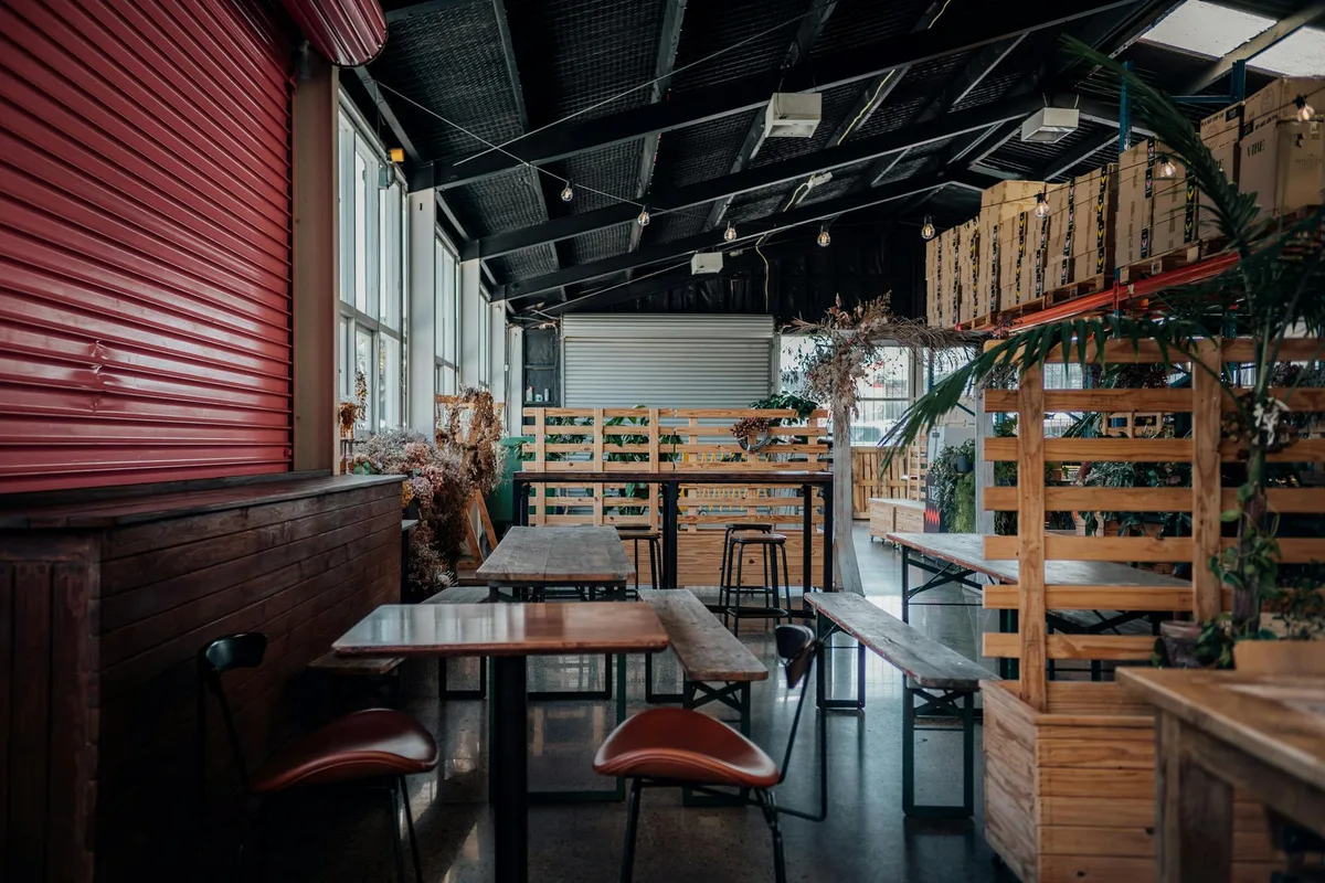 Cafeteria industrial aconchegante com assentos de madeira, plantas e iluminação moderna