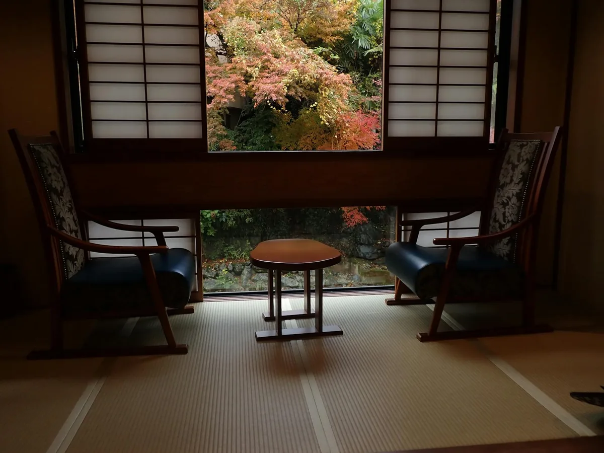 Gemütliches japanisches Zimmer mit Tatami-Matten, Stühlen und Gartenblick durch Shoji-Fenster
