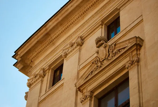 Vista detalhada de uma fachada de edifício barroco com esculturas ornamentadas e céu claro de verão.