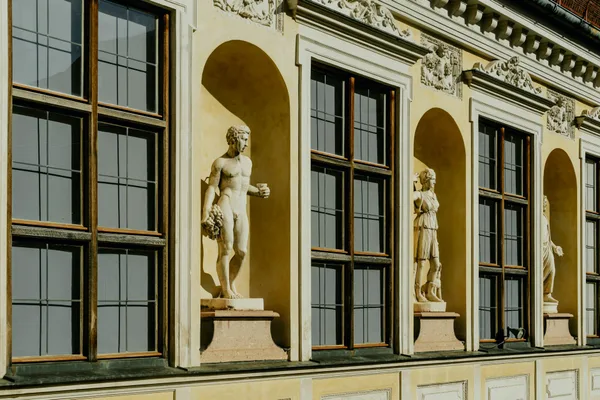 Vista detalhada de uma fachada de edifício clássico adornada com estátuas ornamentadas e janelas amplas.