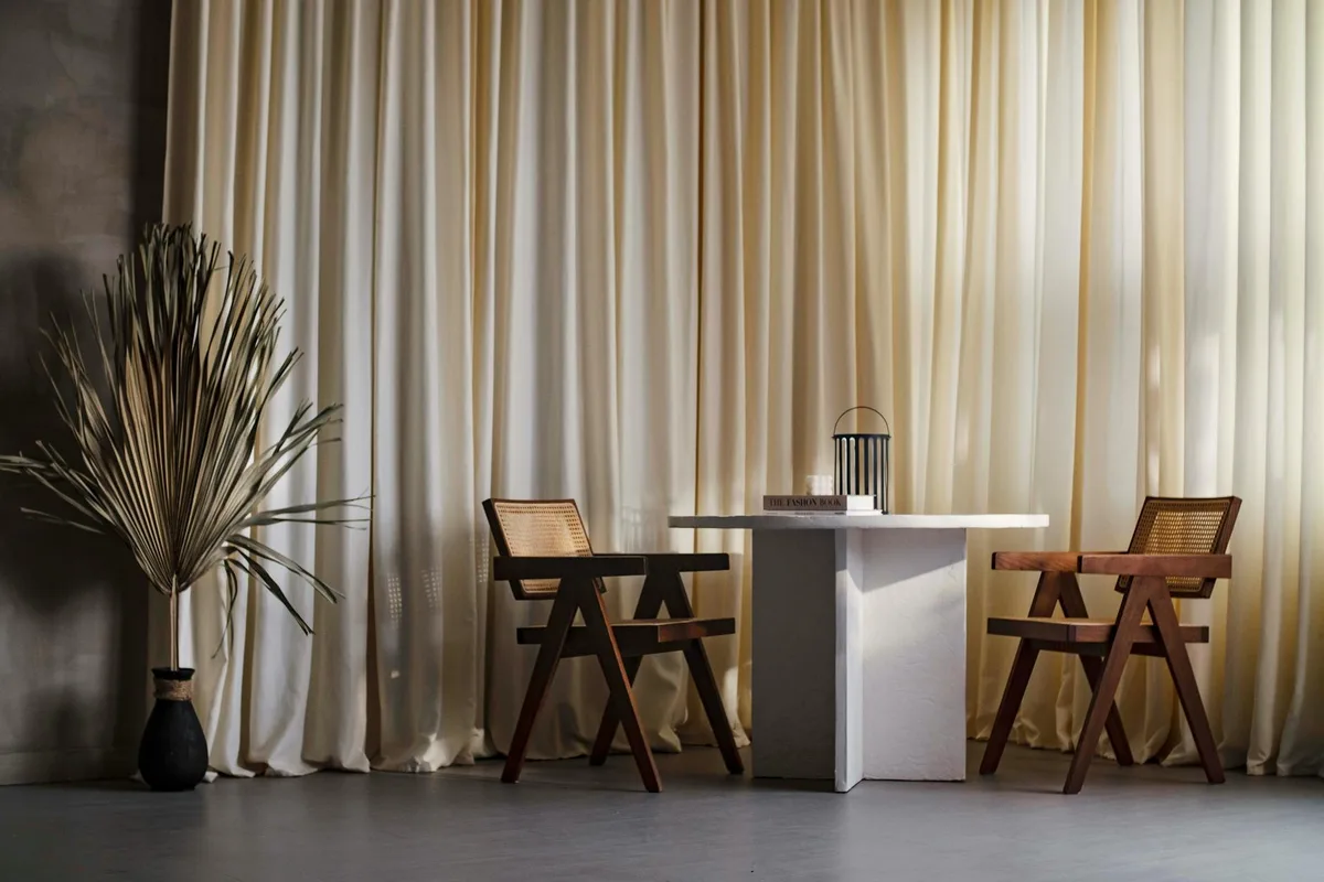 Interior elegante estilo Japandi com poltronas de madeira, mesa branca e cortinas neutras