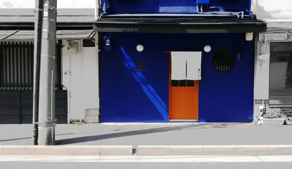 Facciata blu vibrante a Kyoto con tenda noren tradizionale e porta in legno in giornata di sole