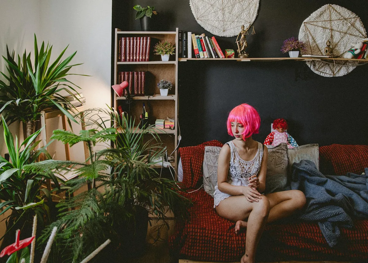 Frau mit pinker Perücke in eklektischem Raum mit Pflanzen und Büchern