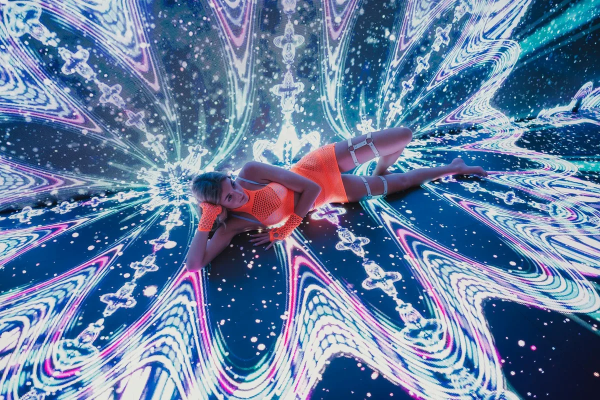 Ballerina in abito neon vibrante su palco digitale con motivi luminosi dinamici