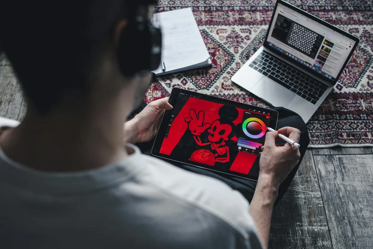 Person zeichnet auf einem Tablet mit Laptop in der Nähe, digitale Kunstschöpfung zu Hause