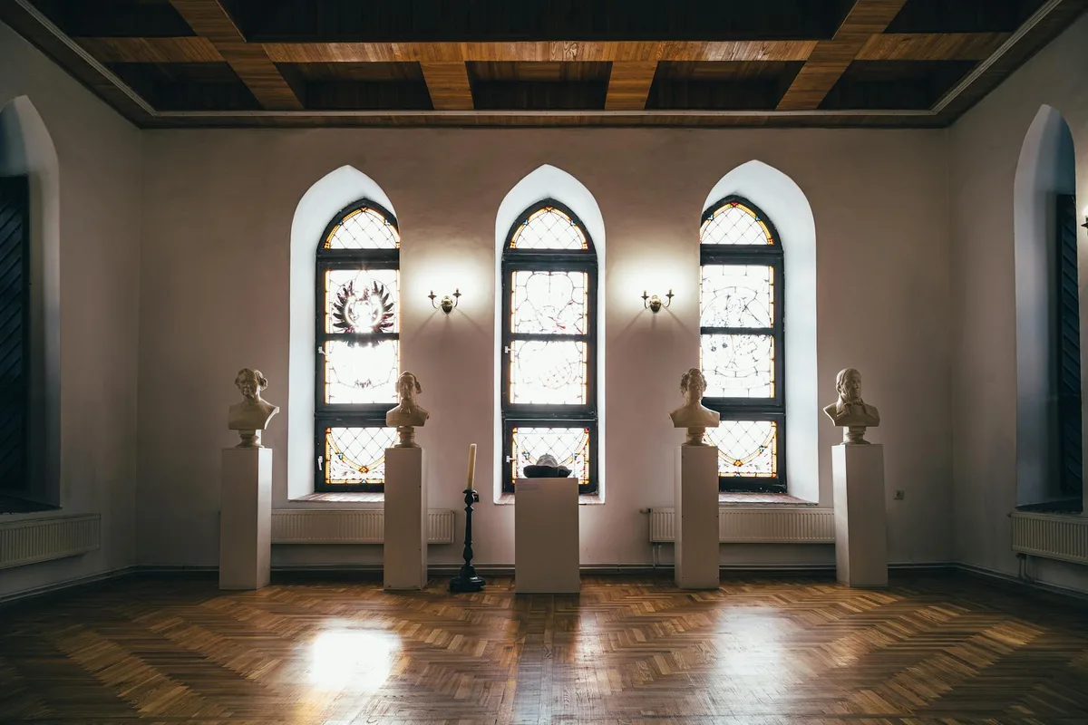 Sala de museu sofisticada com bustos de mármore e vitrais.