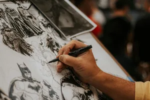 Artist drawing detailed comic book characters with a pen at a lively event.