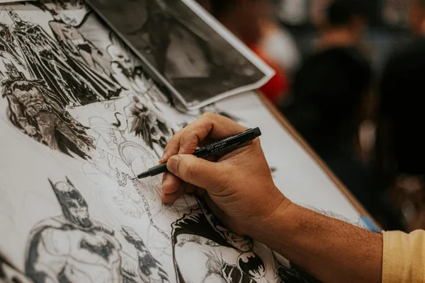 Artist drawing detailed comic book characters with a pen at a lively event.