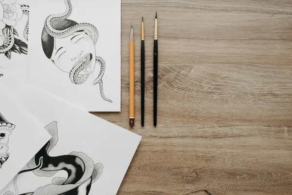 Artistic flat lay featuring pencil sketches and brushes on a wooden surface, perfect for creative content.