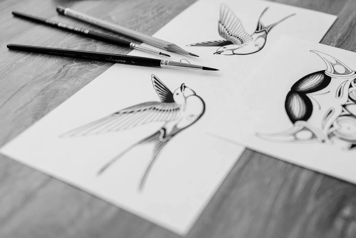 Schwarz-weiße Kunstskizzen von Vögeln mit Zeichenwerkzeugen auf einem Holzschreibtisch mit Nahaufnahme-Detail