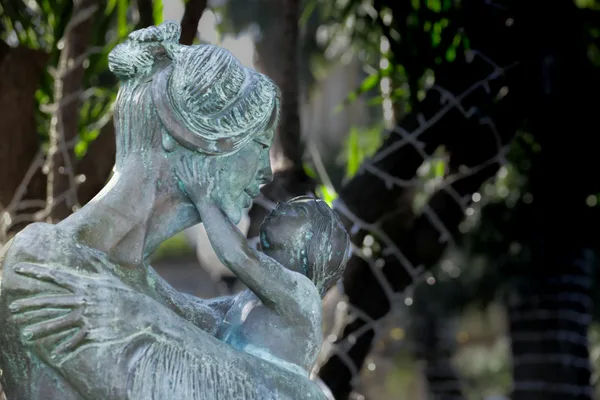 Primo piano di una scultura in bronzo raffigurante una madre che abbraccia il suo bambino all'aperto