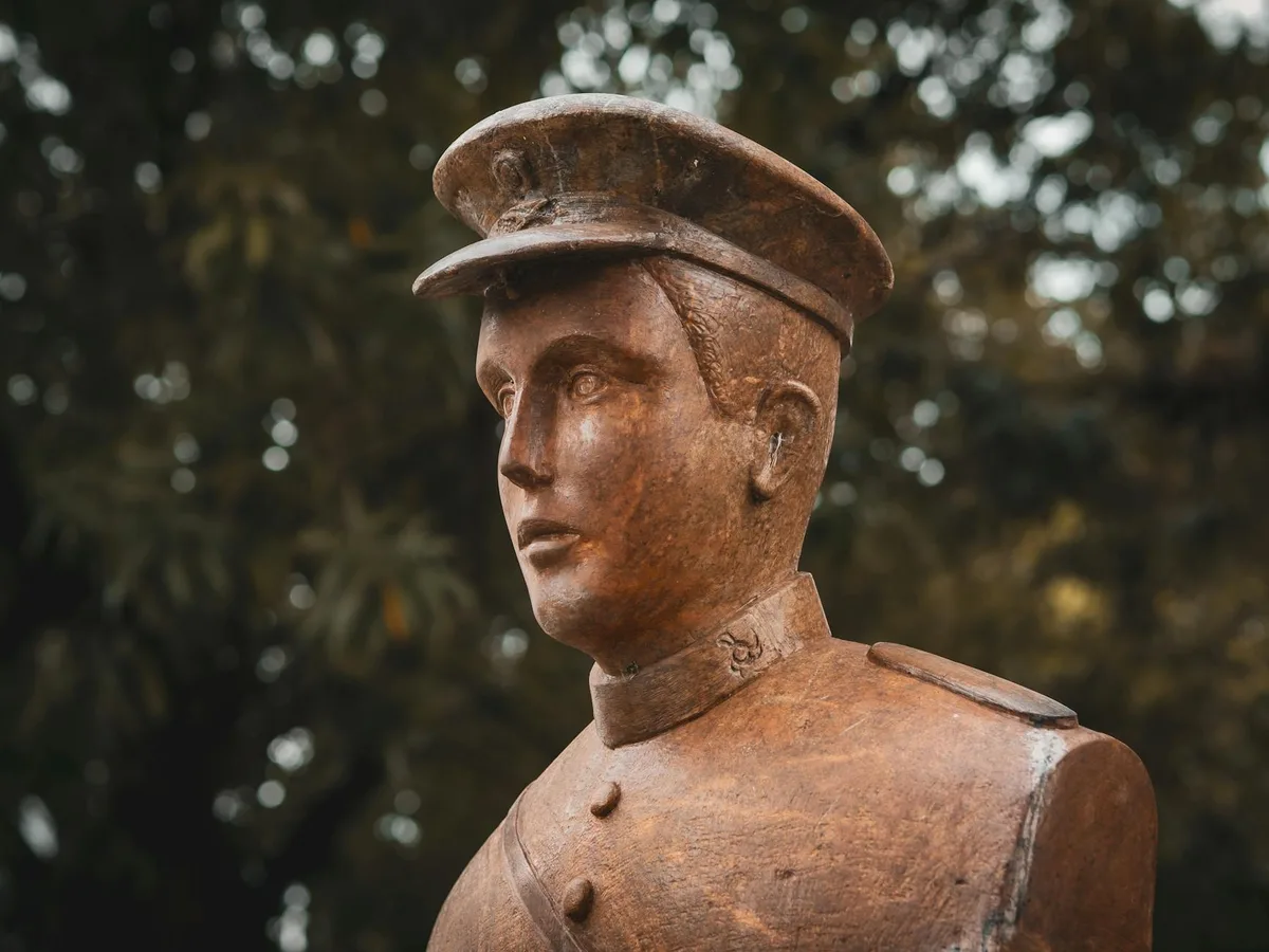 Primo piano statua soldato bronzo con uniforme dettagliata e berretto su sfondo fogliame