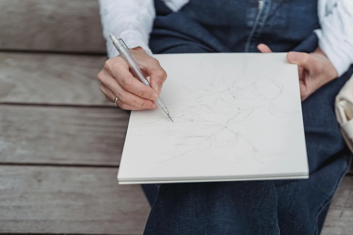 Nahaufnahme einer Person, die draußen in ein Notizbuch zeichnet und Kreativität in Bewegung einfängt