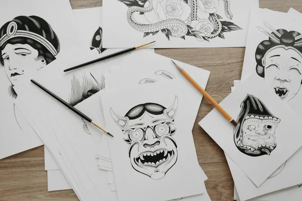 Close-up view of traditional tattoo design illustrations on paper with brushes and pencils.