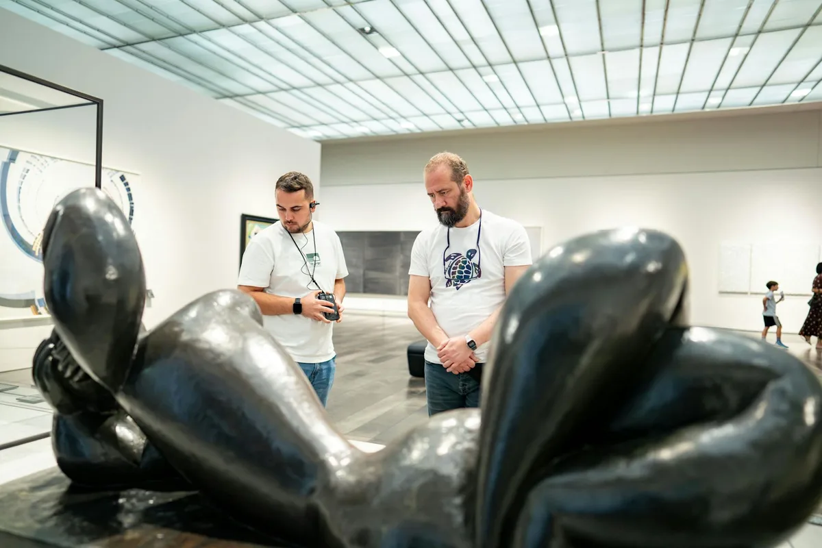 Due uomini osservano una scultura moderna in una galleria d'arte, mostrando apprezzamento artistico