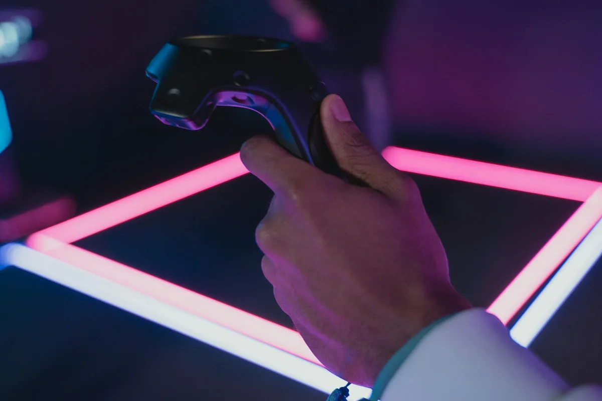 Main tenant une manette VR illuminée par des néons roses et bleus, technologie moderne