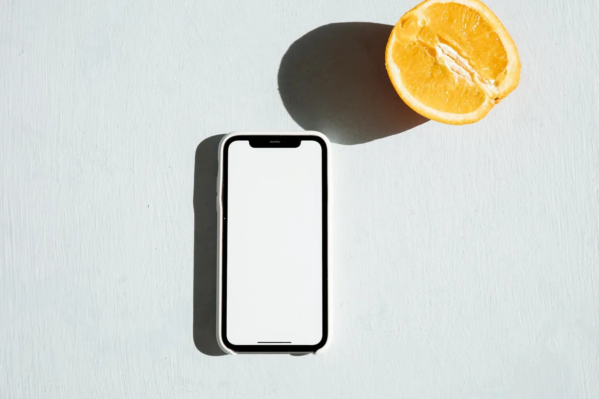 Smartphone mit leerem Bildschirm und Orangenscheibe auf heller Oberfläche als Mockup