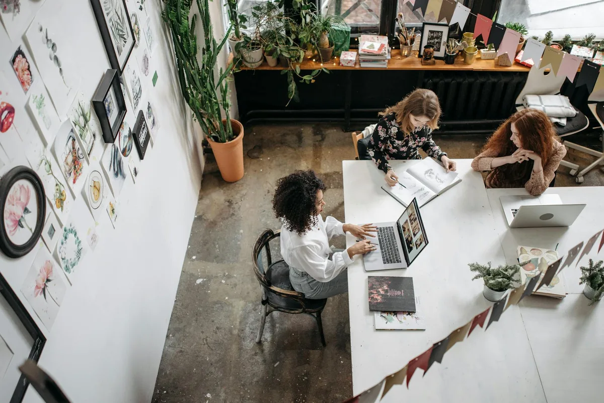 Vogelperspektive auf diverse Frauen bei der Zusammenarbeit in einem stilvollen Büro mit Laptops und Kunstdekor