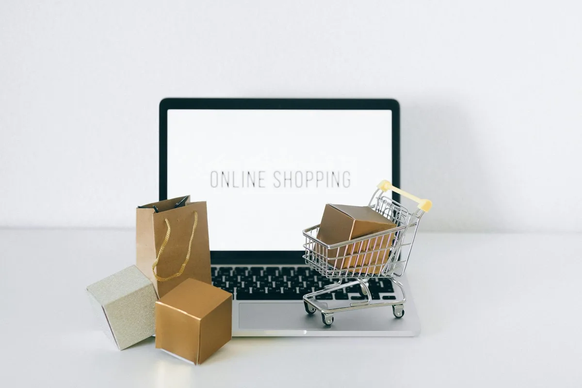 Laptop che mostra acquisti online con scatole e carrello, rappresenta l'ecommerce