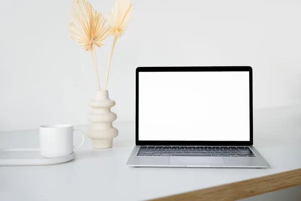 Spazio di lavoro minimalista con laptop piante e tazza su tavolo bianco