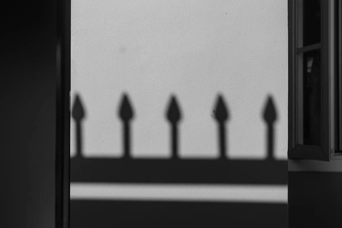 Ombre di recinzione su muro in foto b/n, motivo geometrico