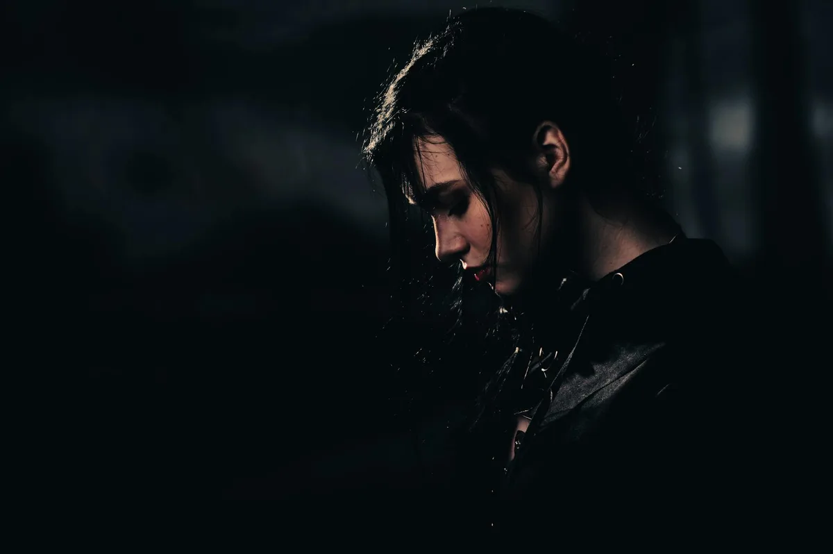 Retrato dramático de mulher com cabelos pretos em ambiente escuro, evocando mistério e contemplação.