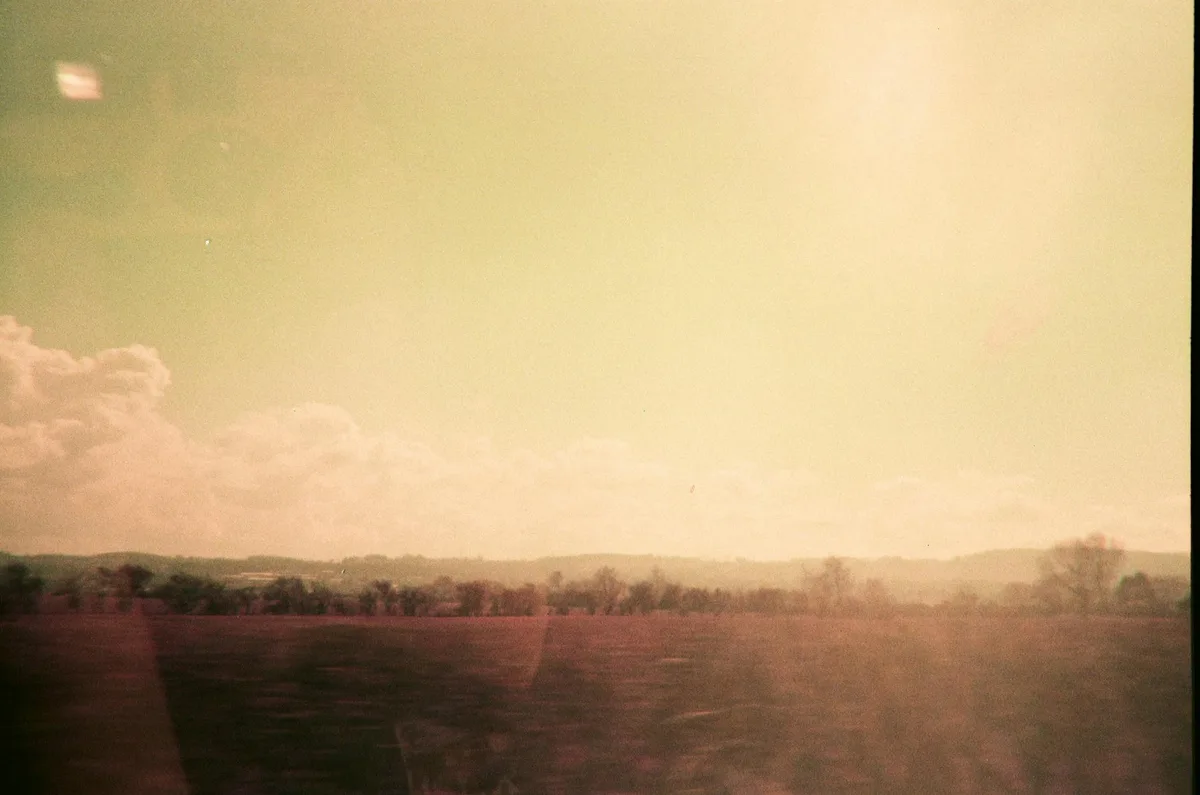Foto analogica sognante di campo velato con nuvole in toni caldi