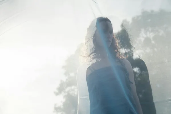 A dreamy portrait of a woman with blurred reflections and sunlight, evoking mystery.
