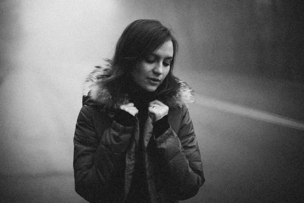 A grayscale portrait of a woman in a fur-lined coat on a foggy winter day.