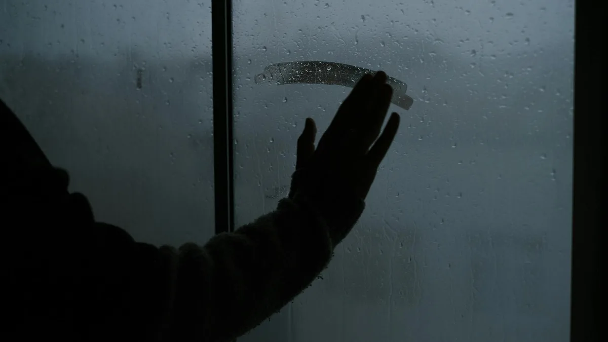 Hand berührt regnerisches, beschlagenes Fenster und schafft melancholische Innenatmosphäre