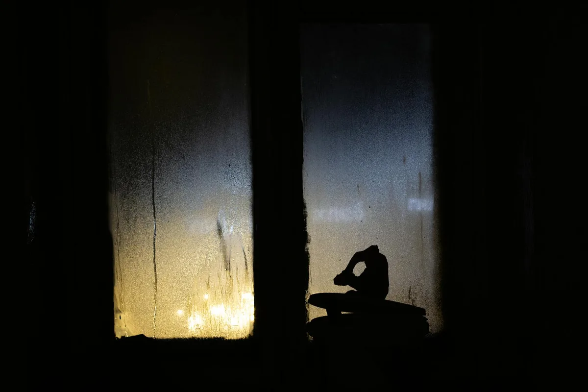 Silhouette vor nassen, neblichen Fenster mit Lichtern bei Nacht.