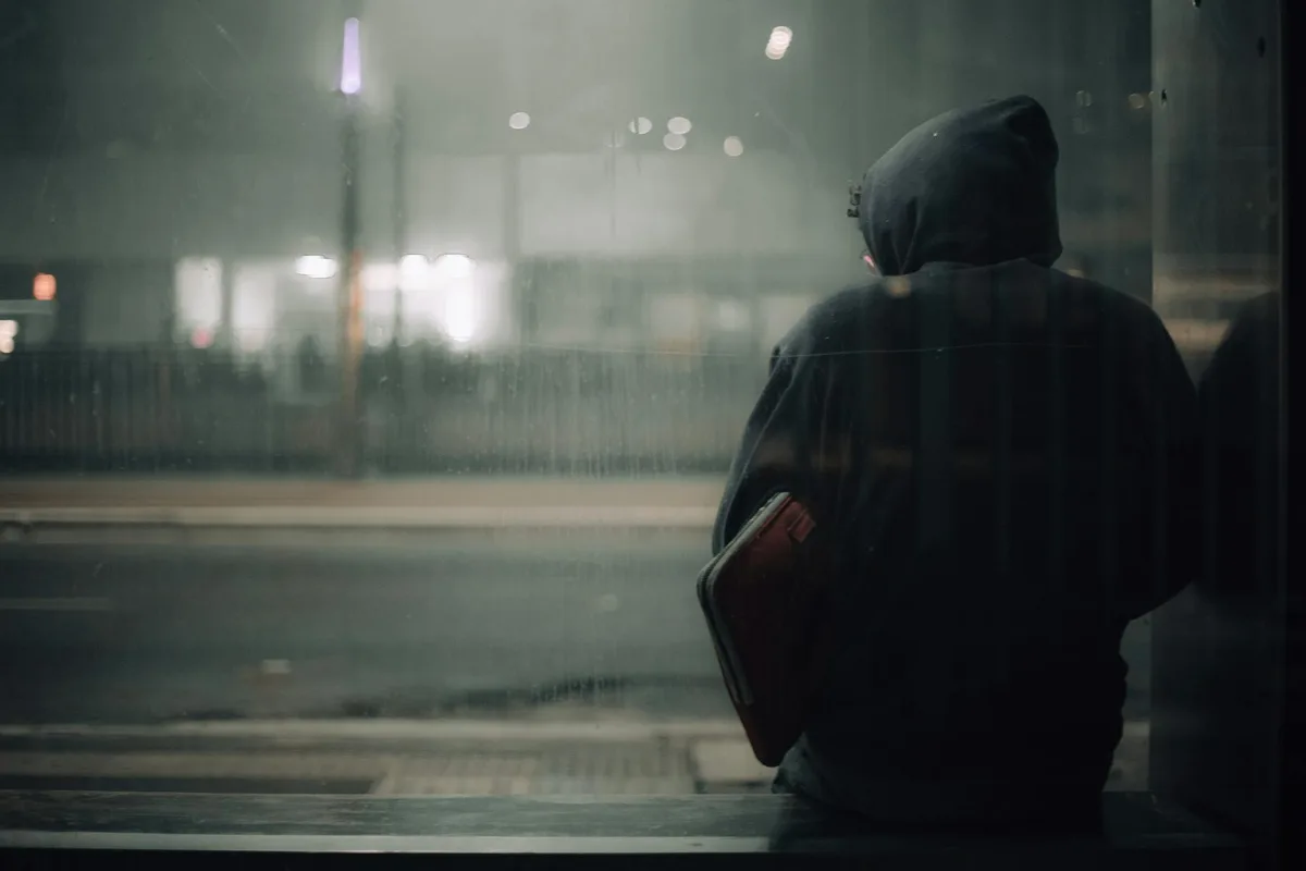 Persona con felpa seduta da sola di notte in riflessione urbana