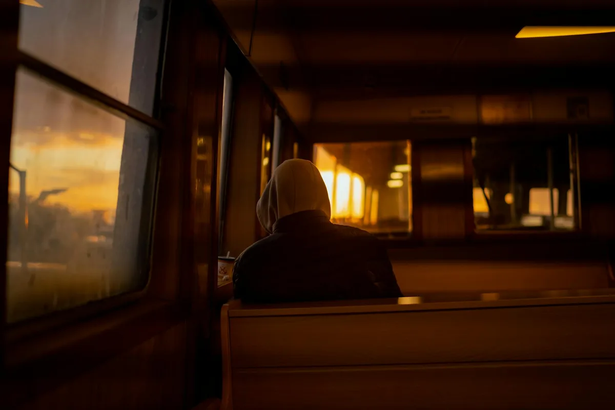 Person sitzt allein in einem Bus und blickt bei Sonnenuntergang aus dem Fenster