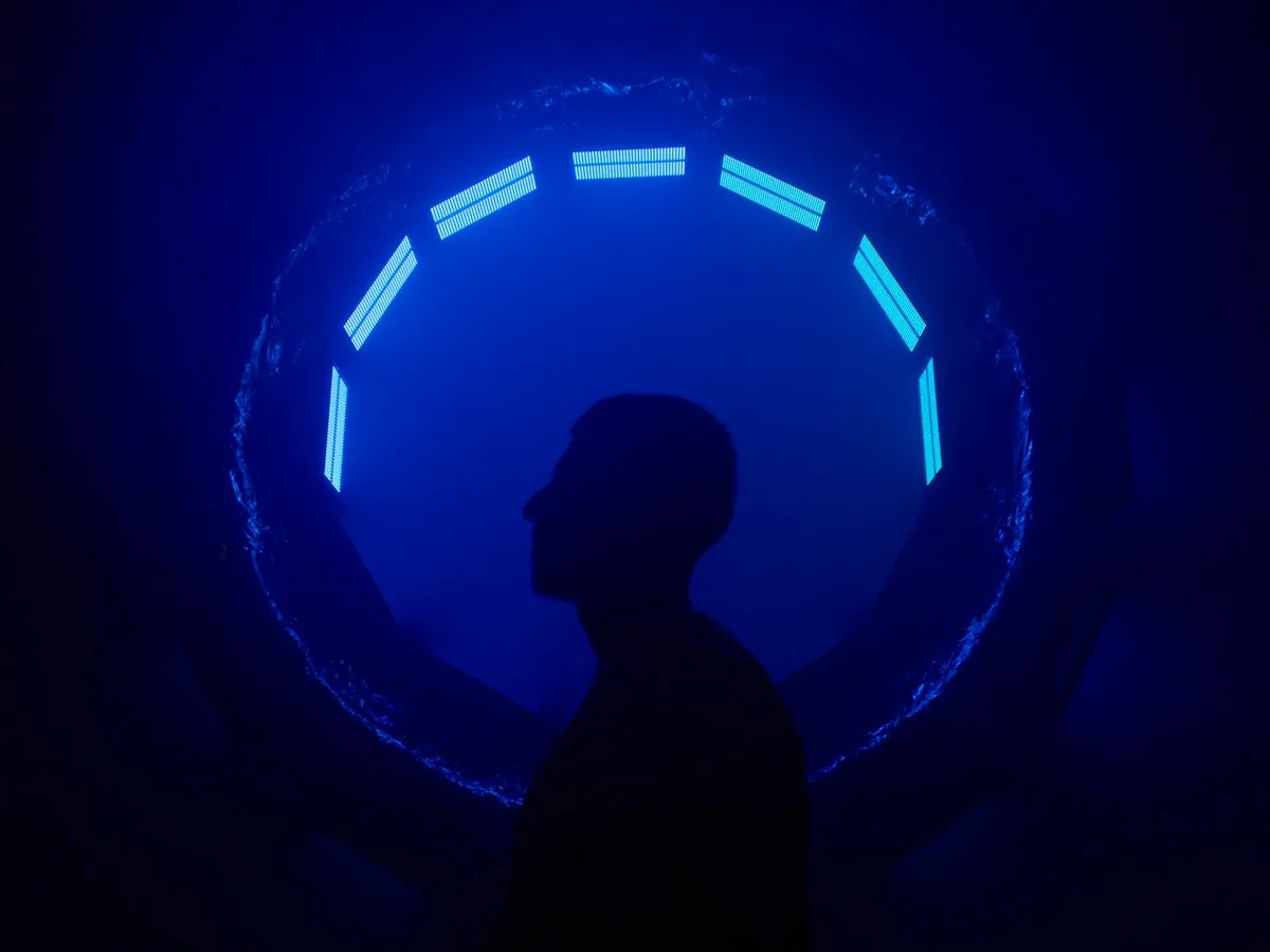 Silhouette di un uomo contro una luce neon blu futuristica che crea un'atmosfera misteriosa.