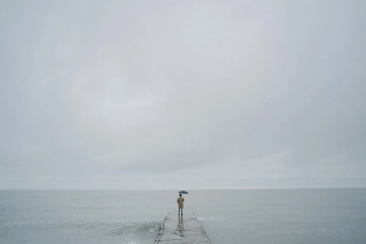 Persona con paraguas en muelle sobre el mar, cielo gris y nublado