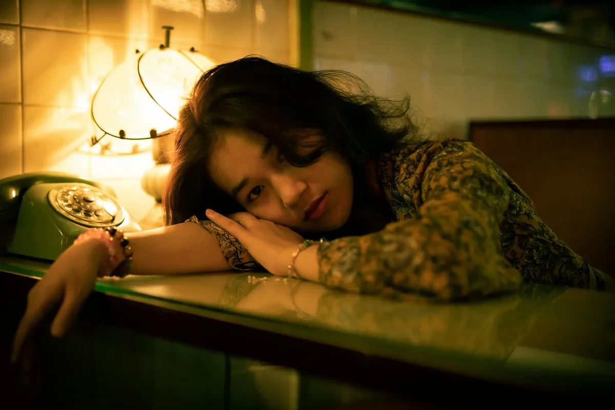 Frau in Blusentop an Glasfläche, beleuchtet von Vintage-Lampe