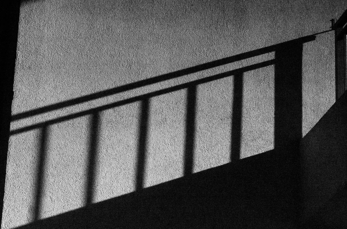 Künstlerischer Schwarz-Weiß-Abstraktschatten von Geländern auf einer strukturierten Wand